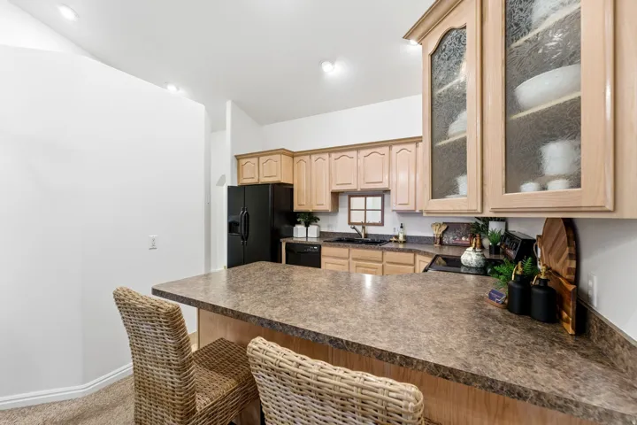 Kitchen featuring a peninsula counter with stone-finish surfacing, light wood cabinetry, recessed lighting, and black appliances