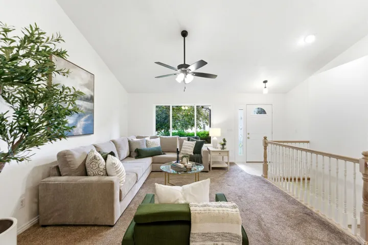 Spacious living area featuring a vaulted ceiling with a ceiling fan, a large window, and light-toned carpeting