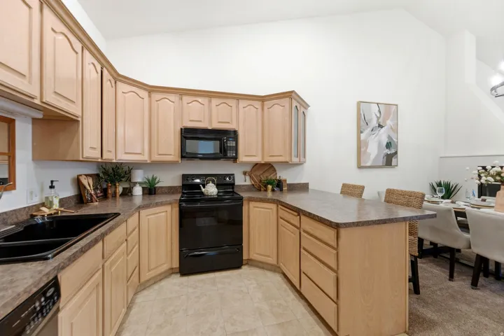 Kitchen featuring light wood cabinetry, dark countertops, built-in microwave, black appliances, and breakfast bar seating