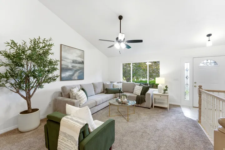 Spacious living area featuring vaulted ceilings, a ceiling fan with integrated lighting, and carpet flooring