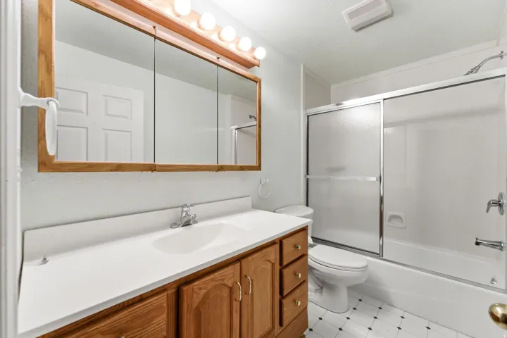 Bathroom featuring a vanity with wood-finish cabinetry and a white countertop, an integrated sink with a chrome faucet, and a large mirror with a wood-finish frame and overhead lighting