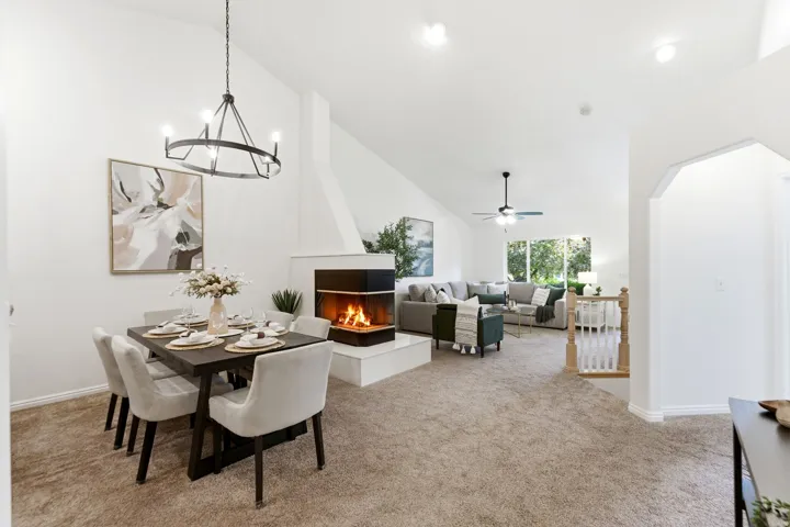 Cathedral ceilings define this living space featuring a central fireplace with a hearth, a contemporary chandelier, and carpeting