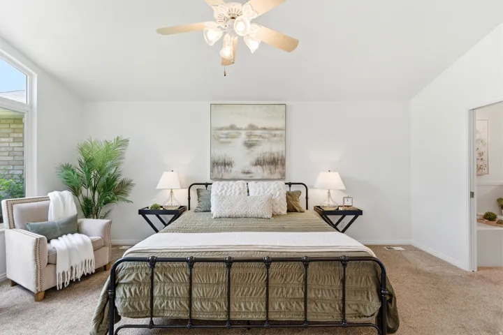 Carpeted bedroom featuring a vaulted ceiling with a ceiling fan, a large window, and light-colored walls
