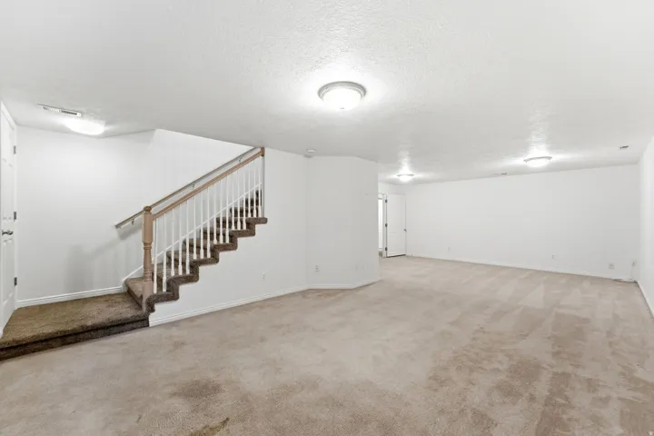 Spacious carpeted room featuring a staircase with wood-finish railing and white balusters