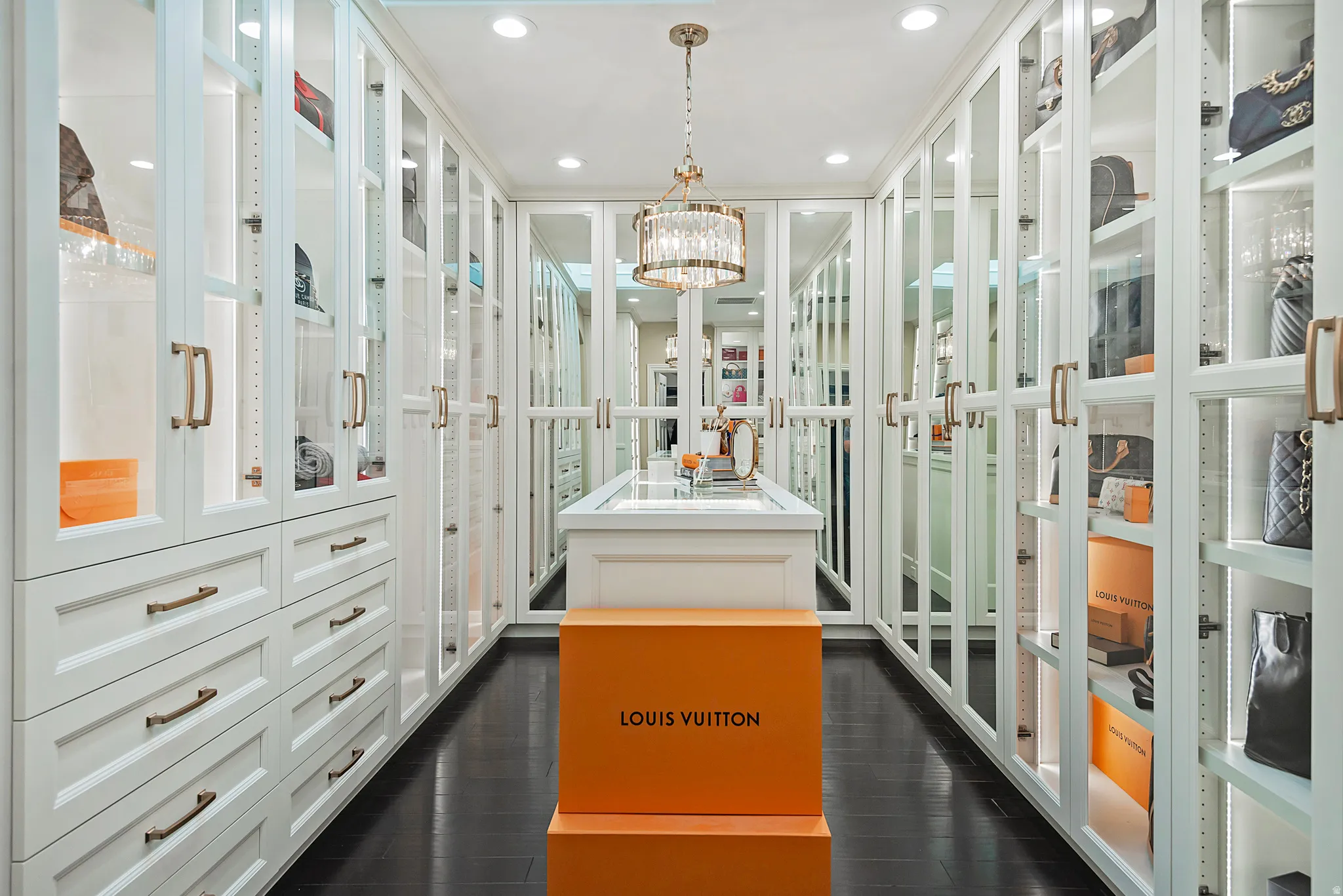 Custom closet featuring extensive built-in cabinetry with glass-front doors, recessed lighting, and a central island with a display top