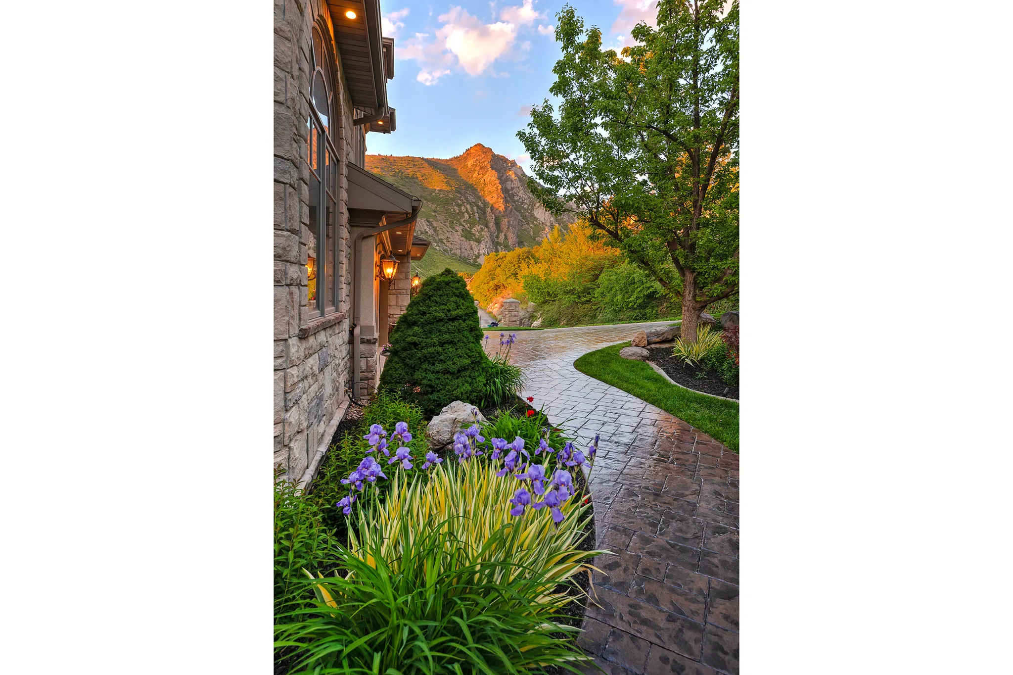 Stone façade with arched window, exterior wall sconces, and a stamped concrete walkway