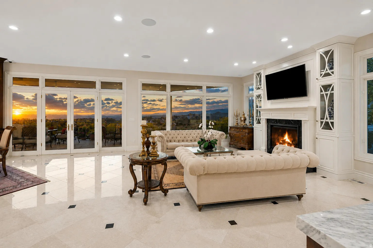 Spacious living area featuring polished tile flooring with contrasting accents, a built-in fireplace with a stone surround, recessed lighting, custom built-in cabinetry with glass inserts, and multiple French doors offering expansive outdoor scenery