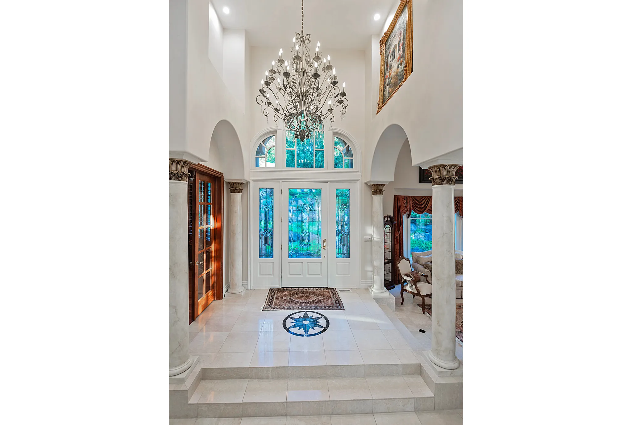 Two-story foyer featuring a grand chandelier, arched doorways, fluted columns, and a custom tile floor medallion