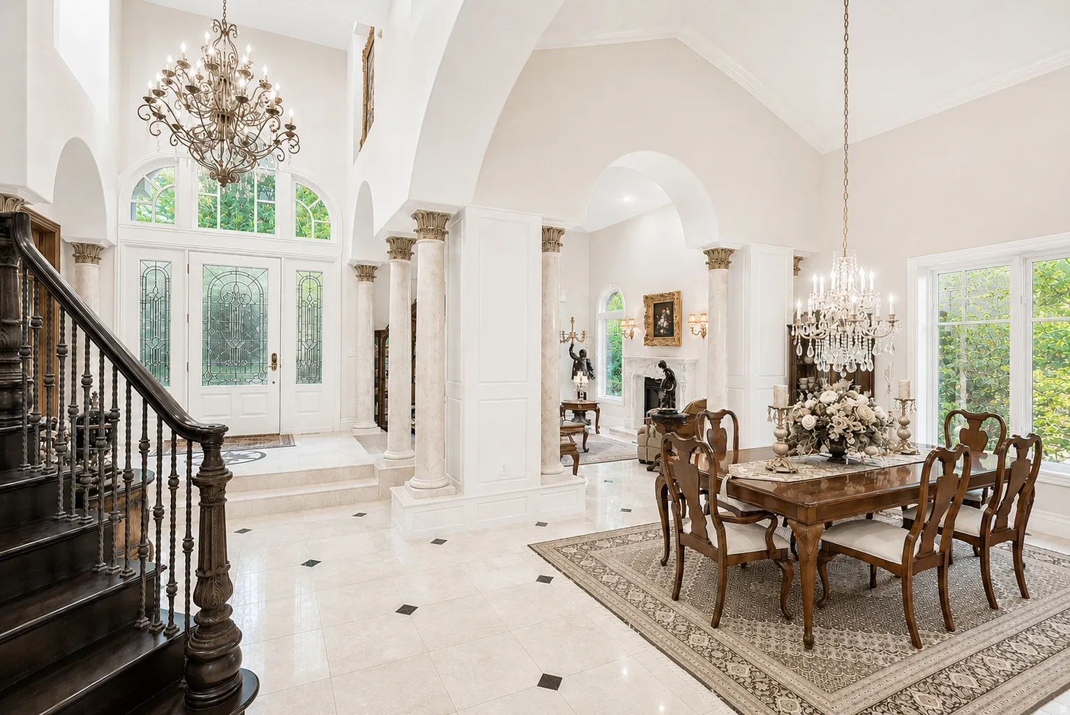 Grand foyer featuring a dark wood staircase with wrought iron balusters, a double-door entry with arched transom windows, and light-toned tile flooring with dark diamond accents