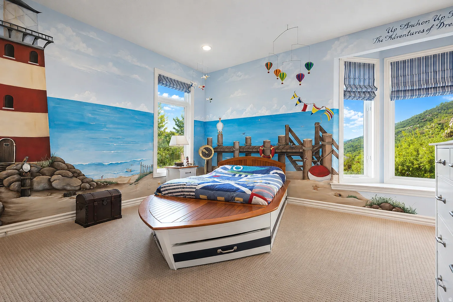 Bedroom featuring extensive nautical-themed wall murals, two large windows with striped Roman shades, and neutral patterned carpeting