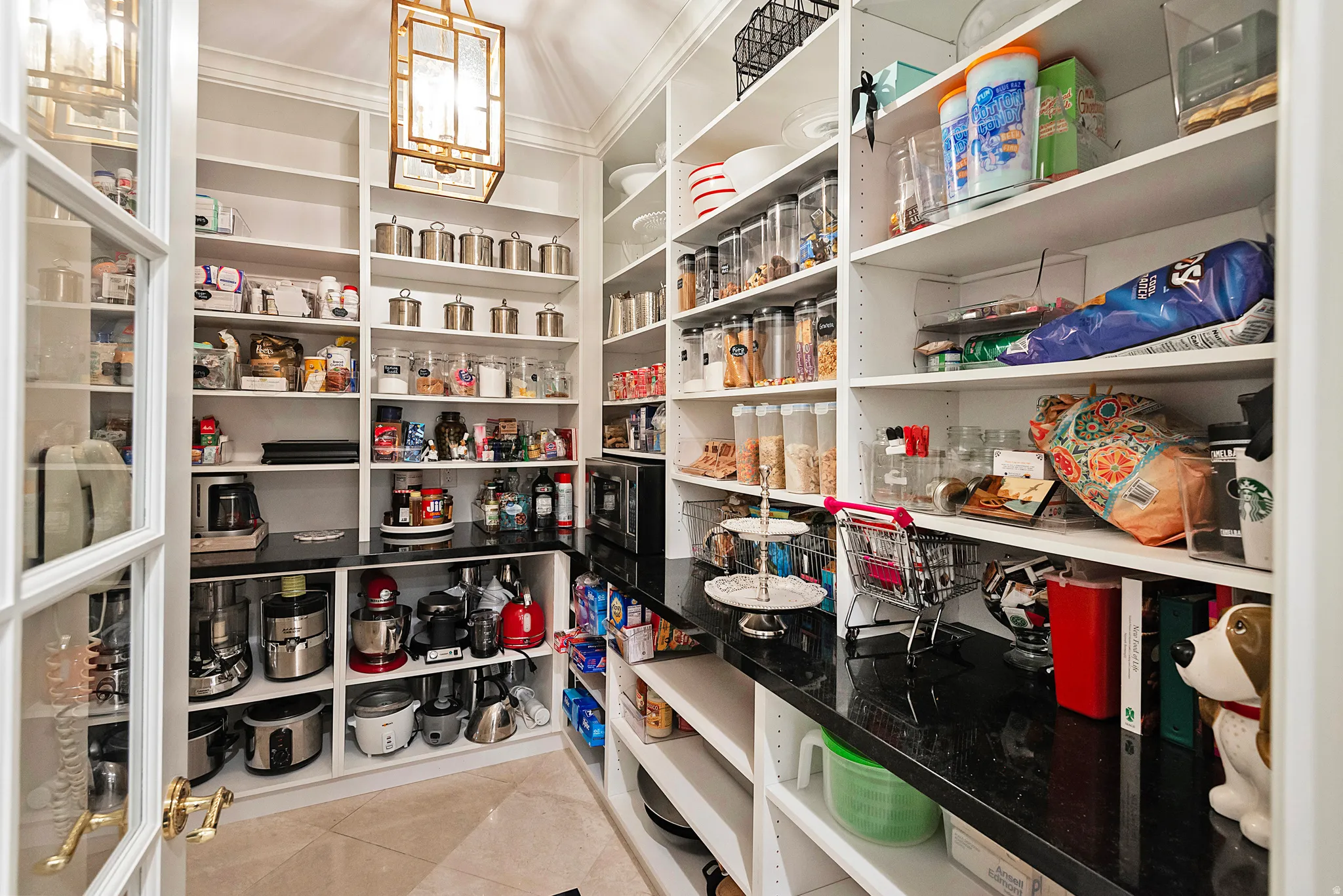 Spacious walk-in pantry featuring extensive built-in shelving, dark countertops, and a decorative ceiling light fixture