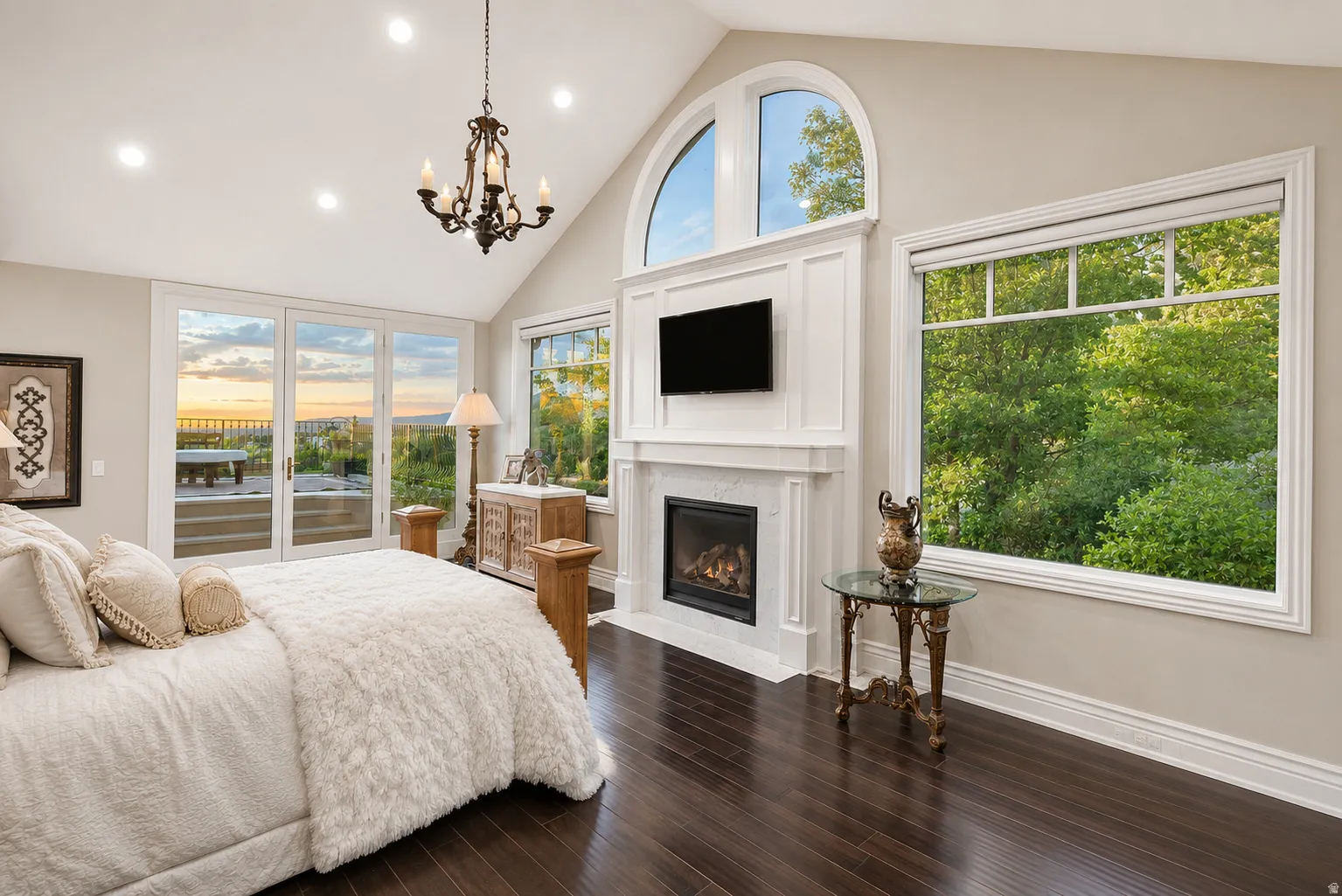 Vaulted ceiling with recessed lighting and a chandelier, engineered wood flooring, three-panel glass door, and a fireplace with a mantel and arched window above