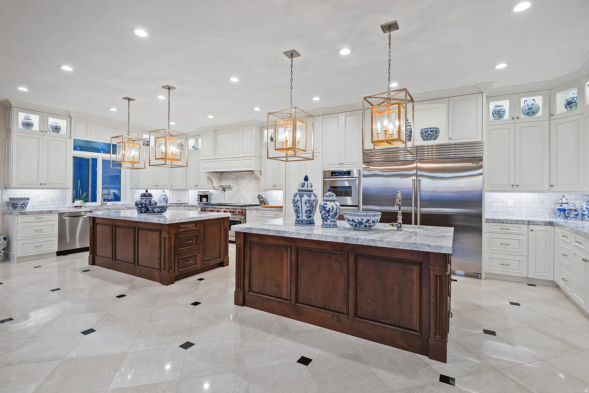 Gourmet kitchen featuring two central islands with stone countertops and wood-panel cabinetry, stainless steel appliances, white perimeter cabinetry, and recessed lighting