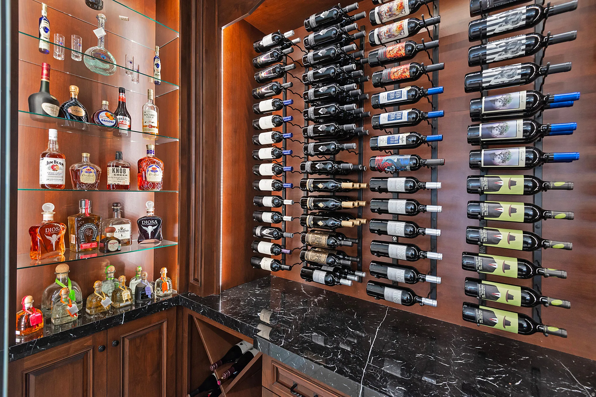 Custom wine storage room featuring warm wood-finish walls, extensive bottle racking, a built-in display cabinet with glass shelving, integrated lighting, and a dark stone-finish countertop