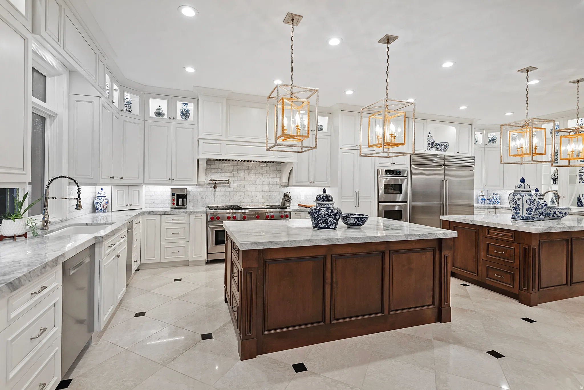 Gourmet kitchen with two wood-paneled islands featuring stone countertops, stainless steel appliances, and white cabinetry