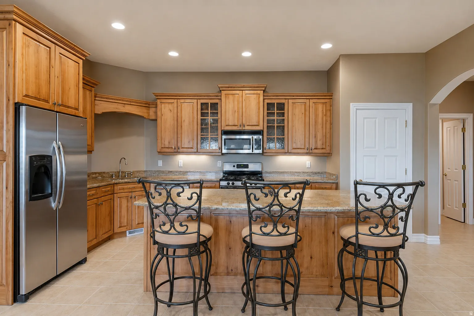 Kitchen featuring light wood cabinetry, granite countertops, stainless steel appliances, and a central island with bar seating