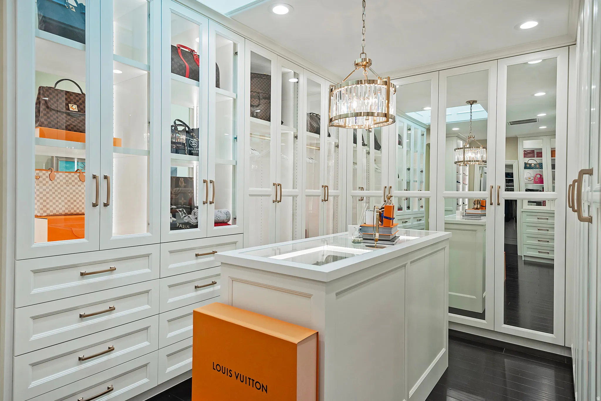 Custom closet system featuring white cabinetry with glass-front display cases and brass hardware