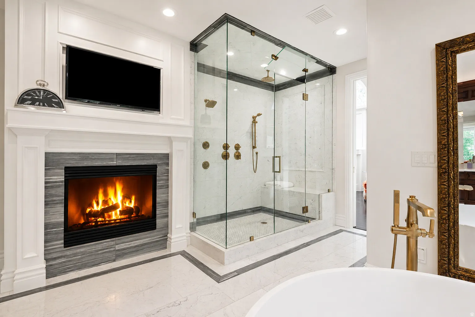 Freestanding glass-enclosed shower with multiple brass fixtures and an integrated bench