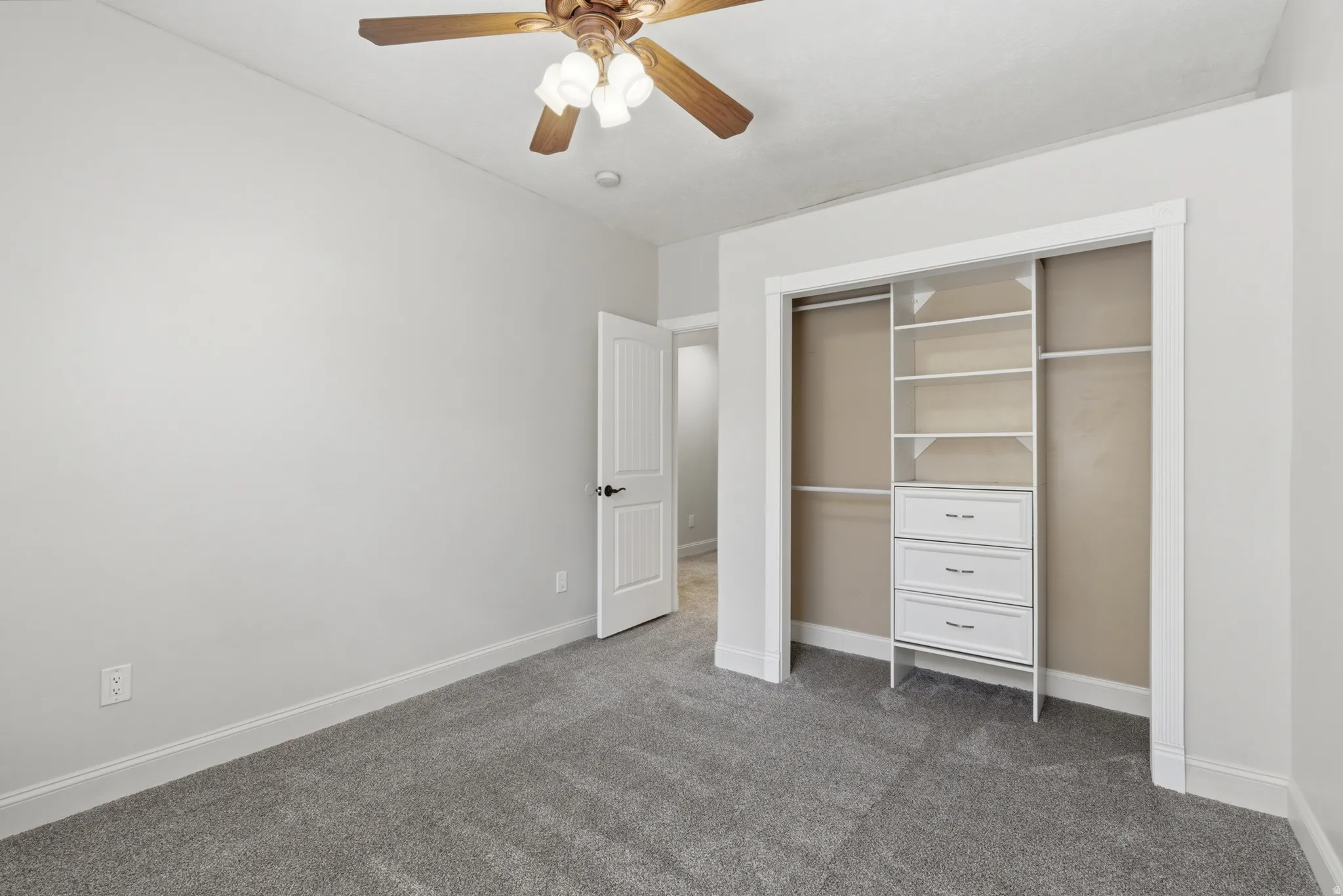 Bedroom featuring gray carpeting, light gray walls, a ceiling fan with light fixture, white trim, and a built-in closet organization system with drawers and shelving