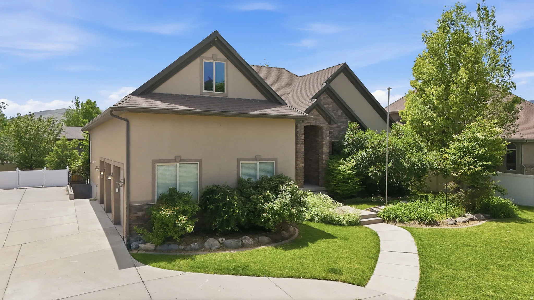 Stucco and stone exterior with a multi-car garage, mature landscaping, and a concrete driveway