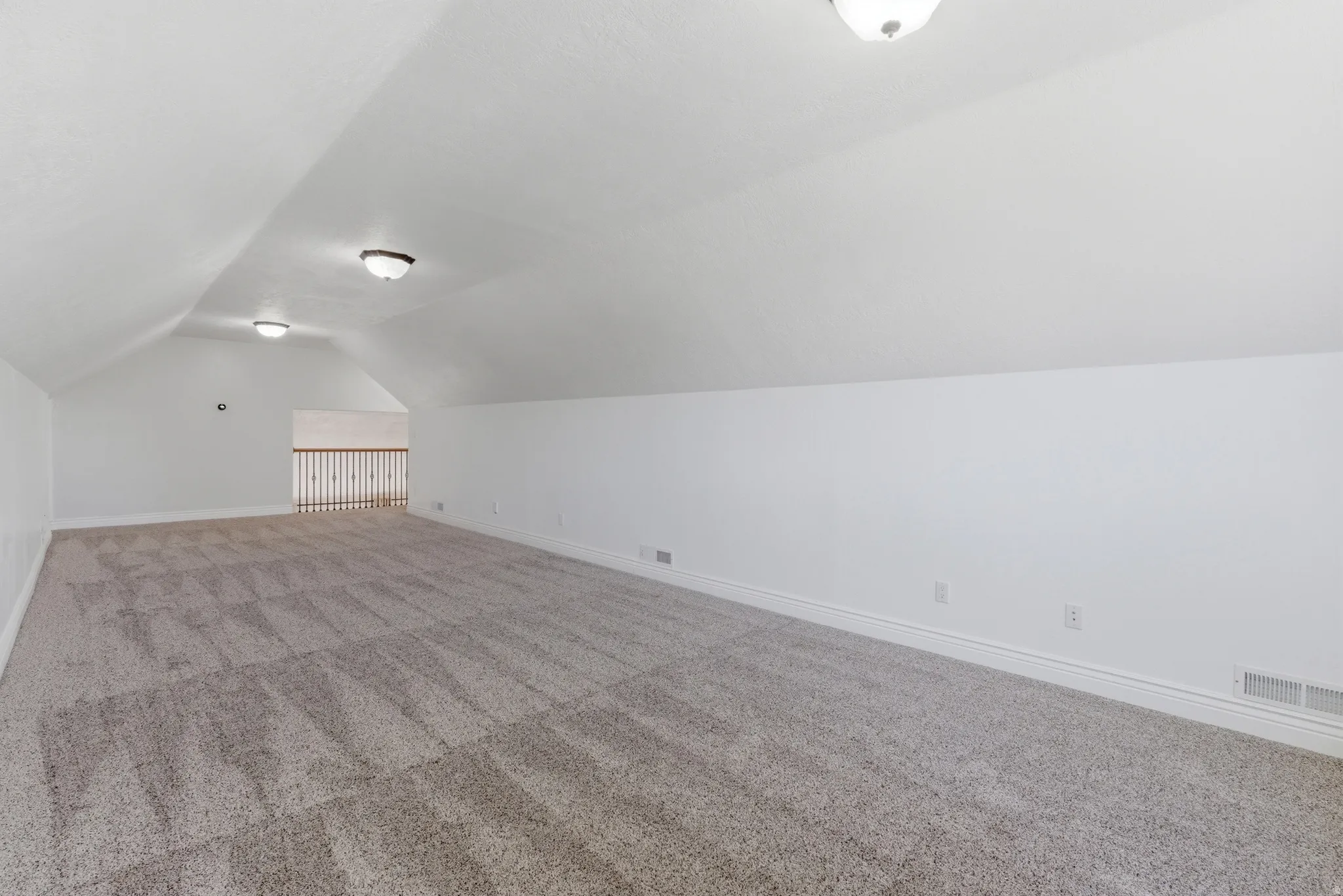 Spacious carpeted room featuring vaulted ceilings, flush mount lighting, a durable railing system, and baseboard trim