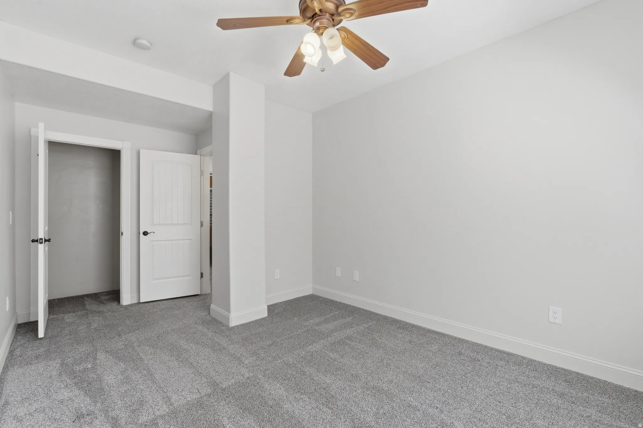 Carpeted room featuring a ceiling fan with light fixture, white interior doors, and a neutral wall color