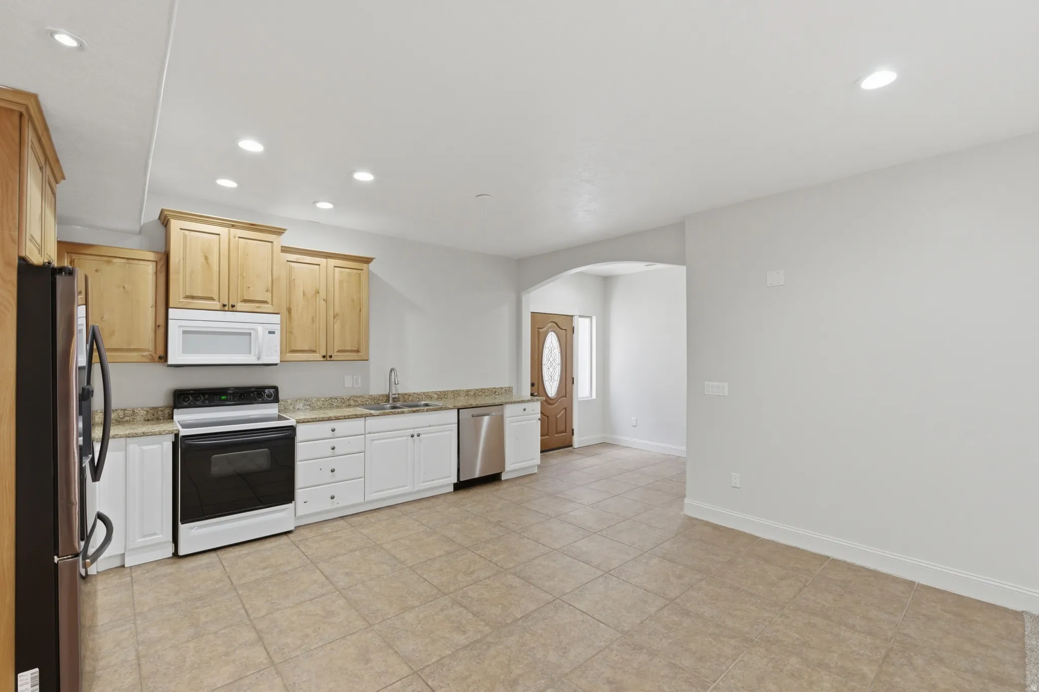 Kitchen featuring a combination of light wood-finish and white cabinetry, a stainless steel sink, and a full suite of appliances including a black and stainless steel refrigerator, black range, white microwave, and stainless steel dishwasher
