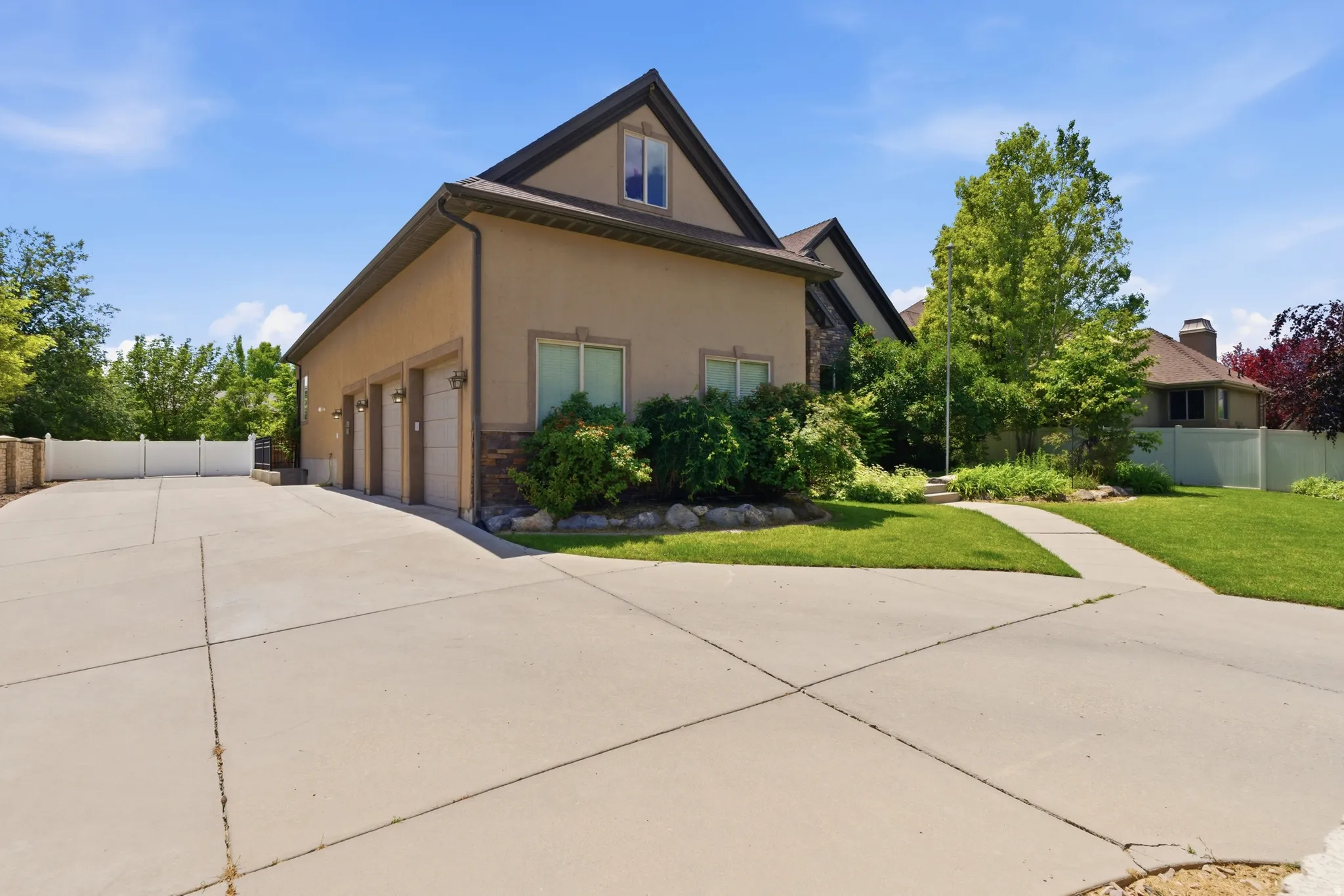 Stucco and stone facade home featuring a three-car garage, dormer window, concrete driveway, and manicured landscaping