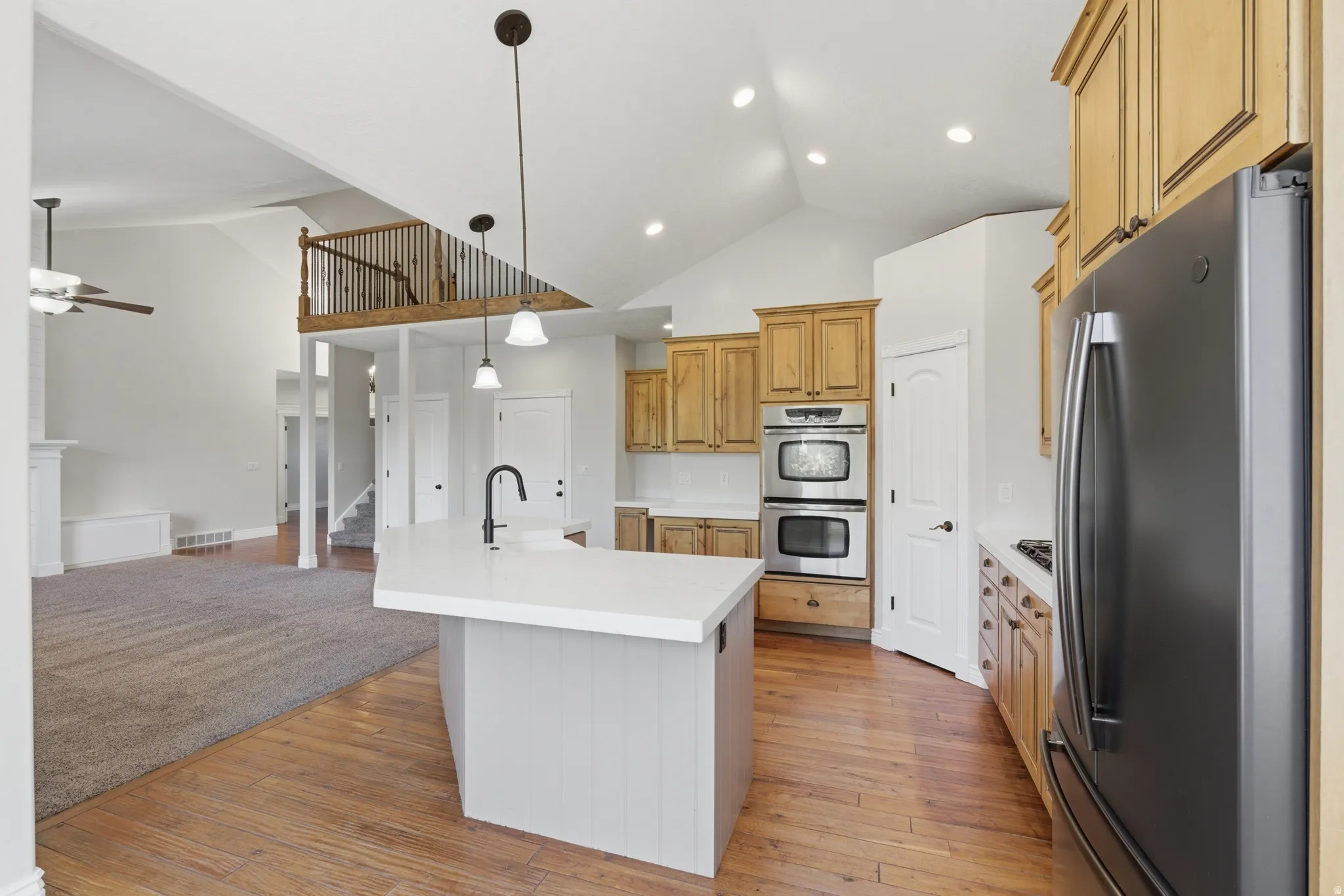 Kitchen featuring a central island with a white countertop and matte black faucet, stainless steel double wall ovens, built-in refrigerator, wood-finish cabinetry, and recessed lighting