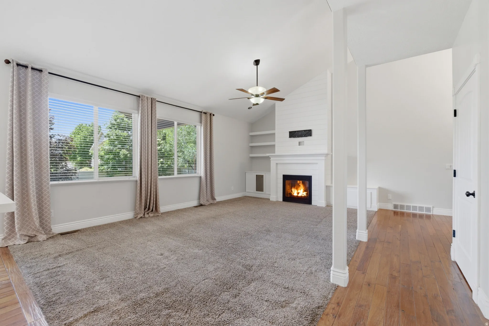 Spacious living area featuring a fireplace with a white mantel, built-in shelving, and a vaulted ceiling with a ceiling fan