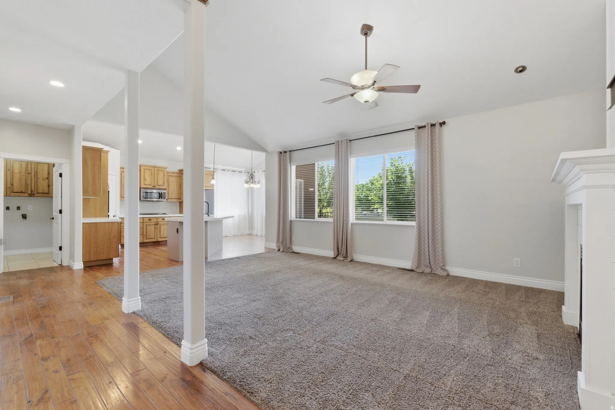 Spacious living area featuring vaulted ceilings, a ceiling fan, plush carpet, and a white fireplace surround