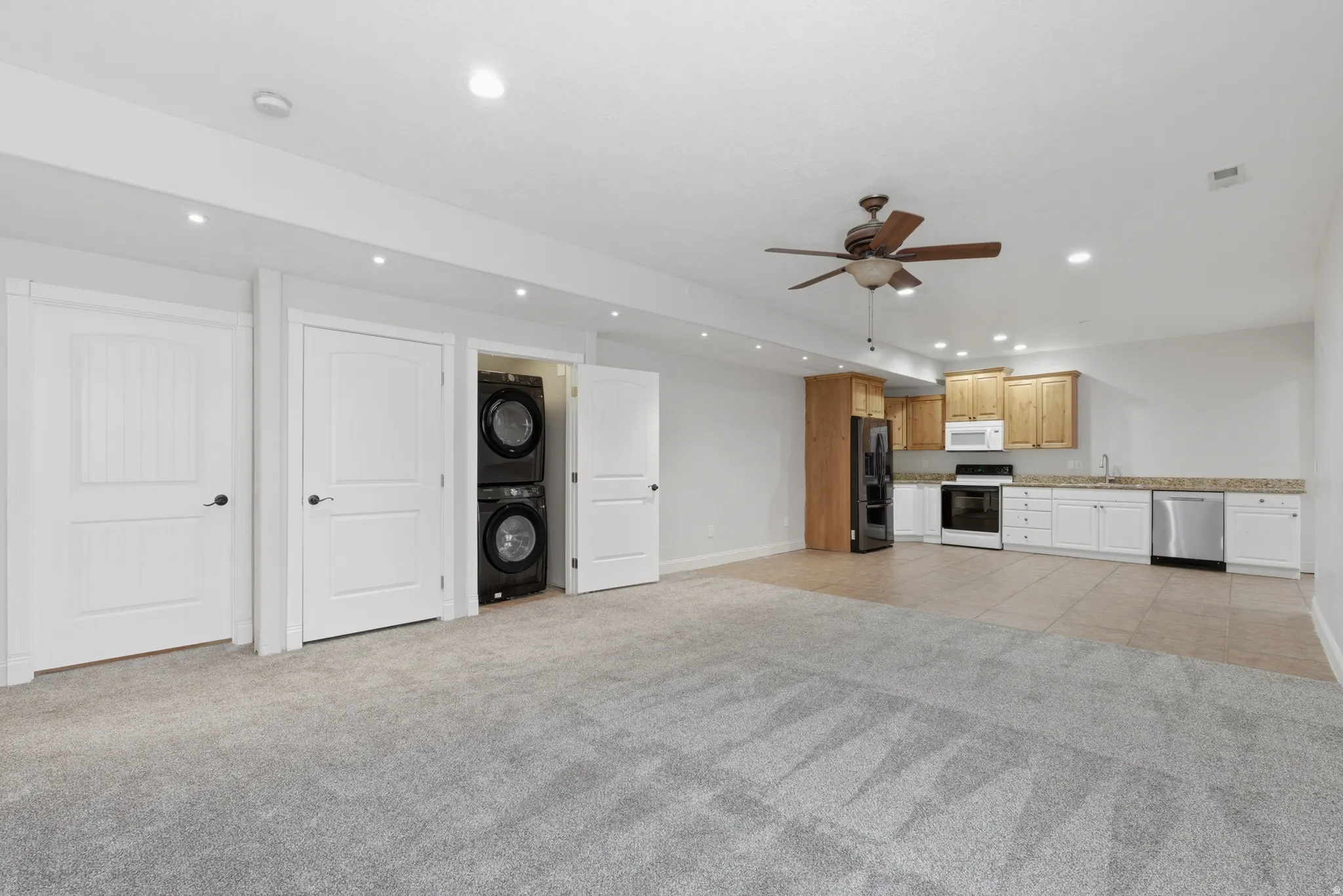Spacious room featuring a compact kitchen with wood cabinetry, stainless steel appliances, and a tile backsplash
