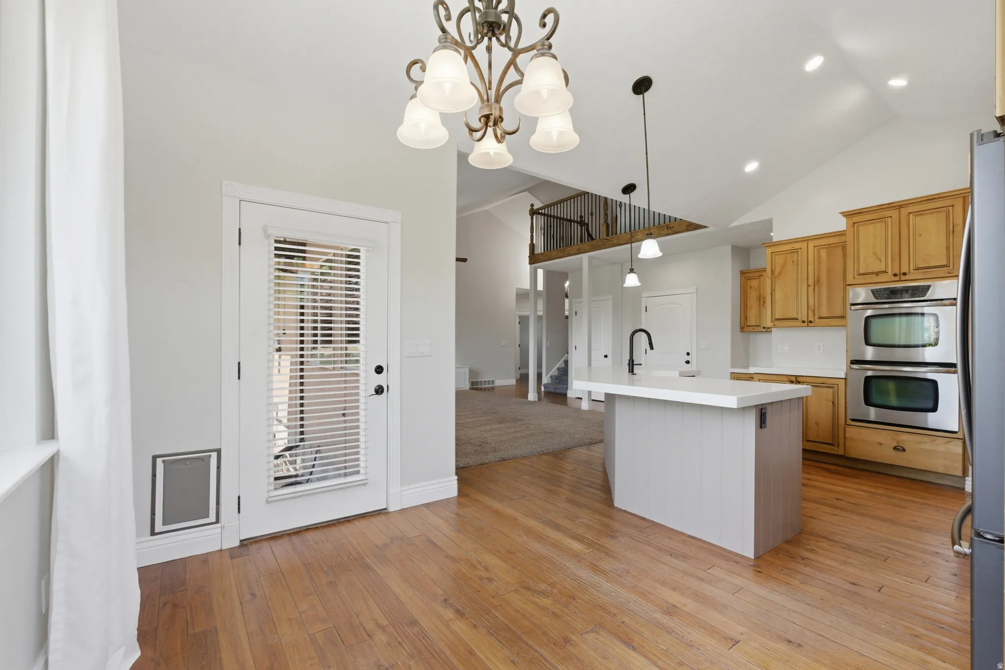 Kitchen featuring wood-finish flooring, light wood cabinetry, stainless steel double ovens, and a center island with a white countertop and pendant lighting