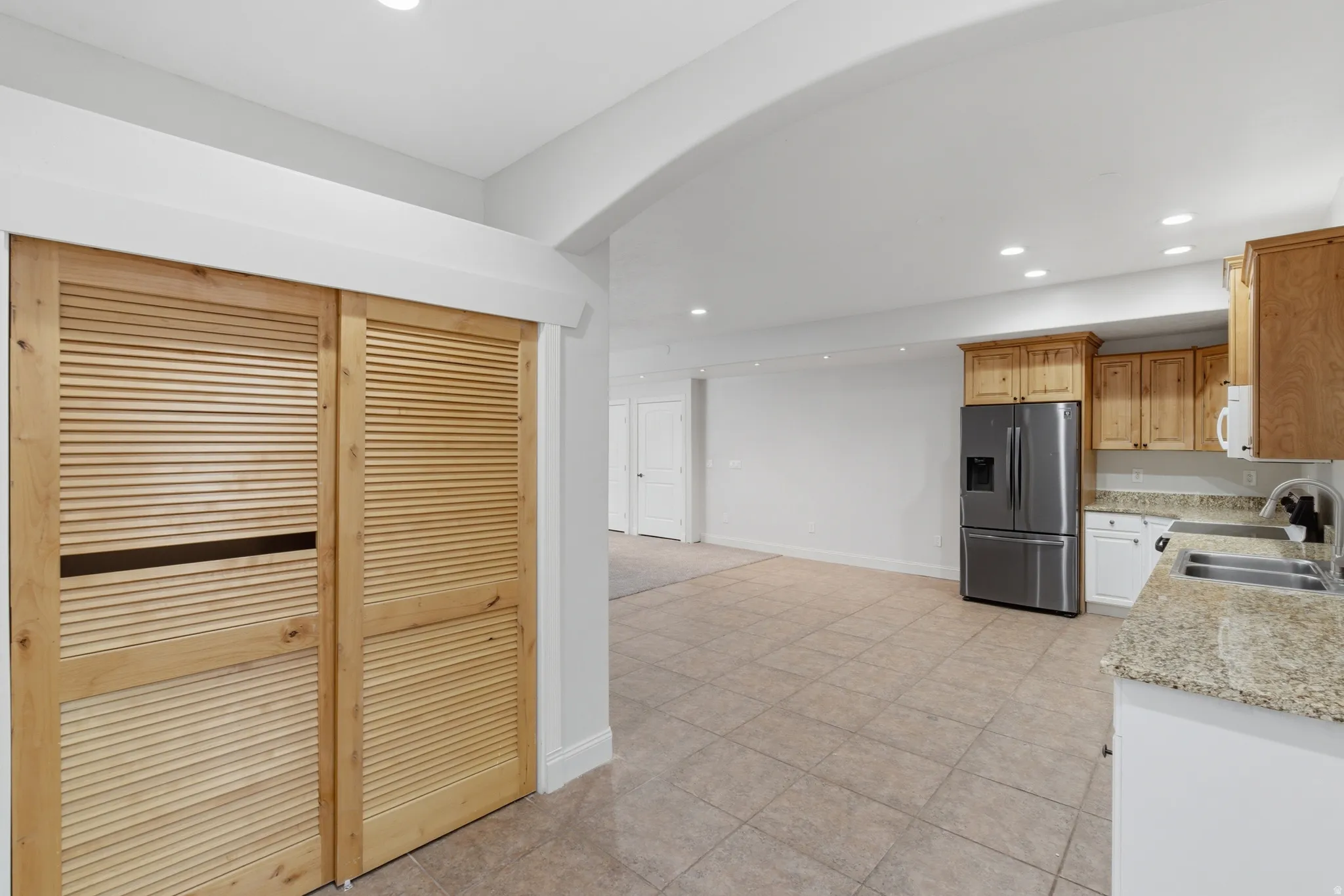 Kitchen area featuring granite countertops, a stainless steel French door refrigerator, wood-finish cabinetry, and recessed lighting