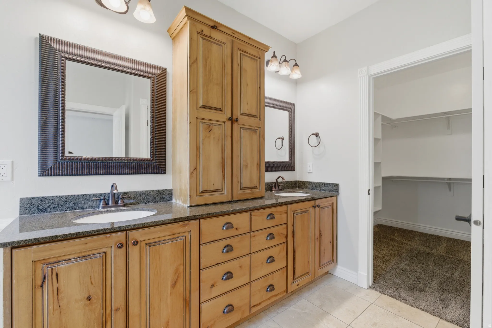 Dual vanity with wood-finish cabinetry, dark countertops, and undermount sinks