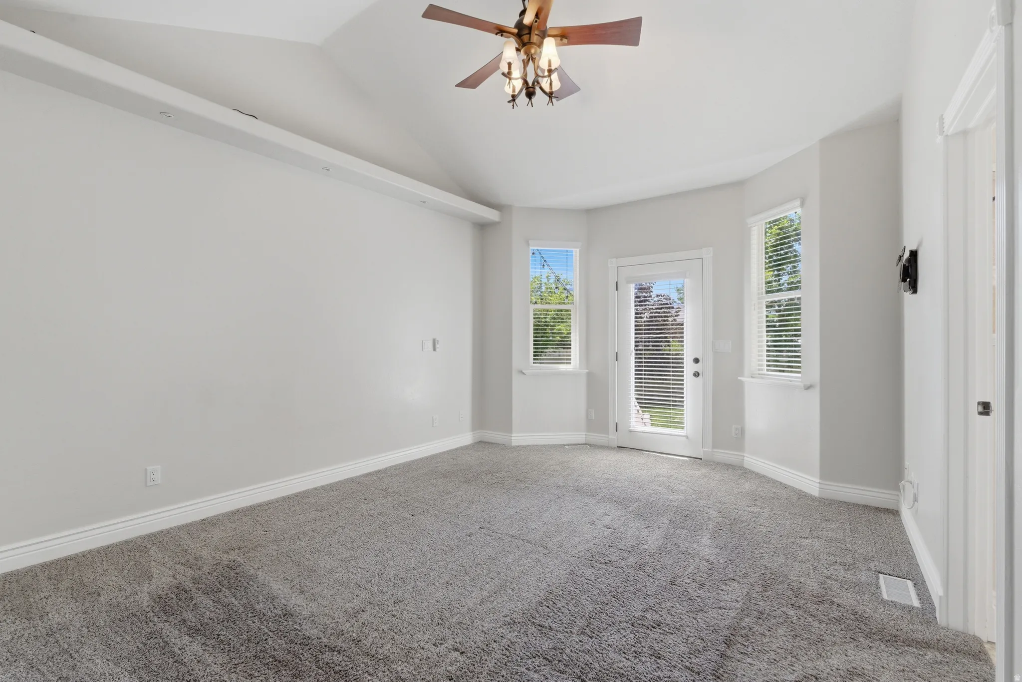 Primary bedroom. Vaulted ceiling with a decorative ceiling fan, carpeting, multiple windows with blinds, and a glass-paneled door