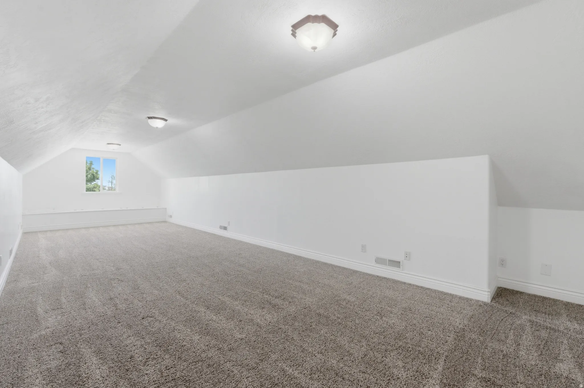 Spacious room featuring vaulted ceilings, neutral-toned carpet, a bright window, and flush-mount lighting fixtures