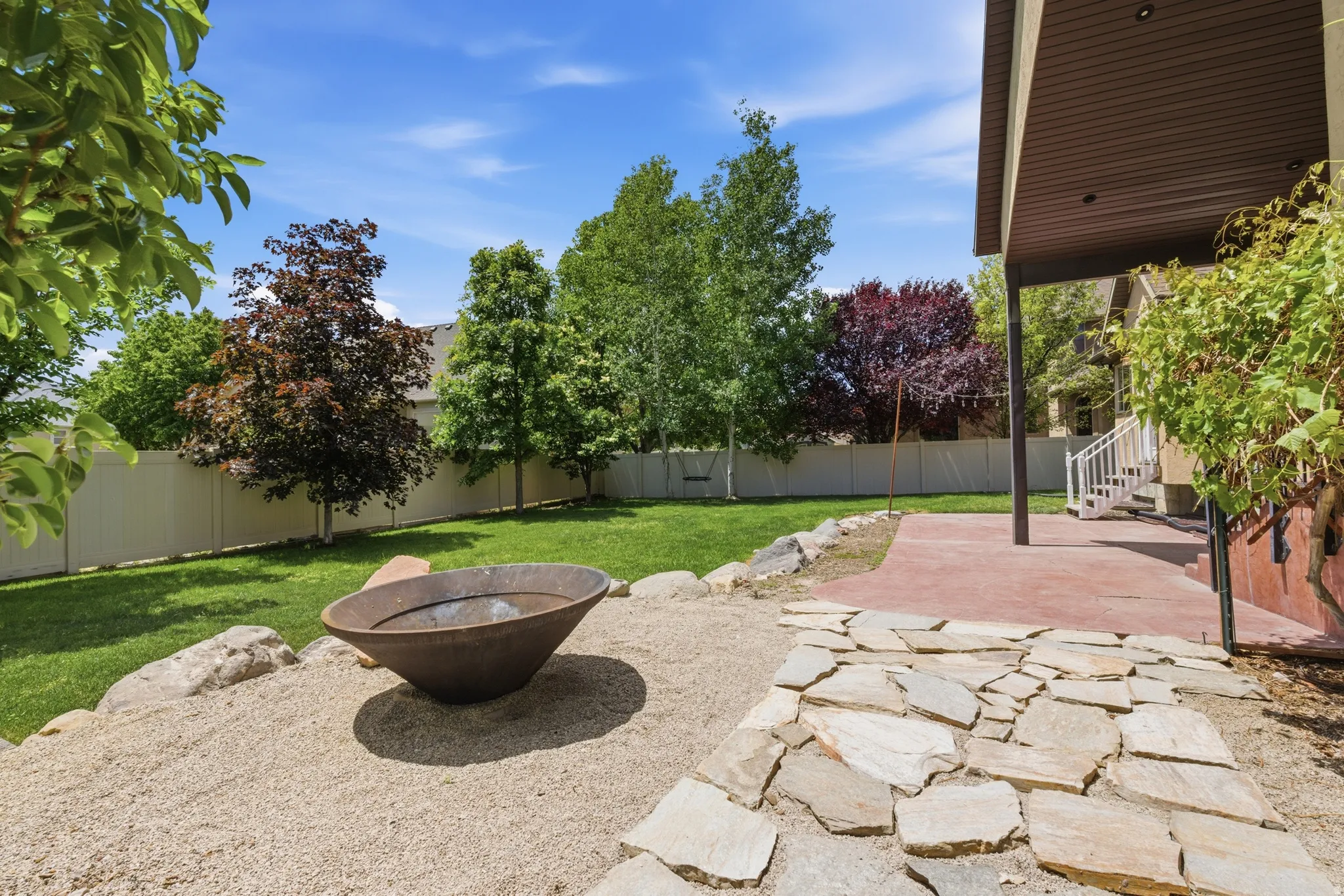 Spacious backyard featuring a large lawn, a white privacy fence, and mature trees