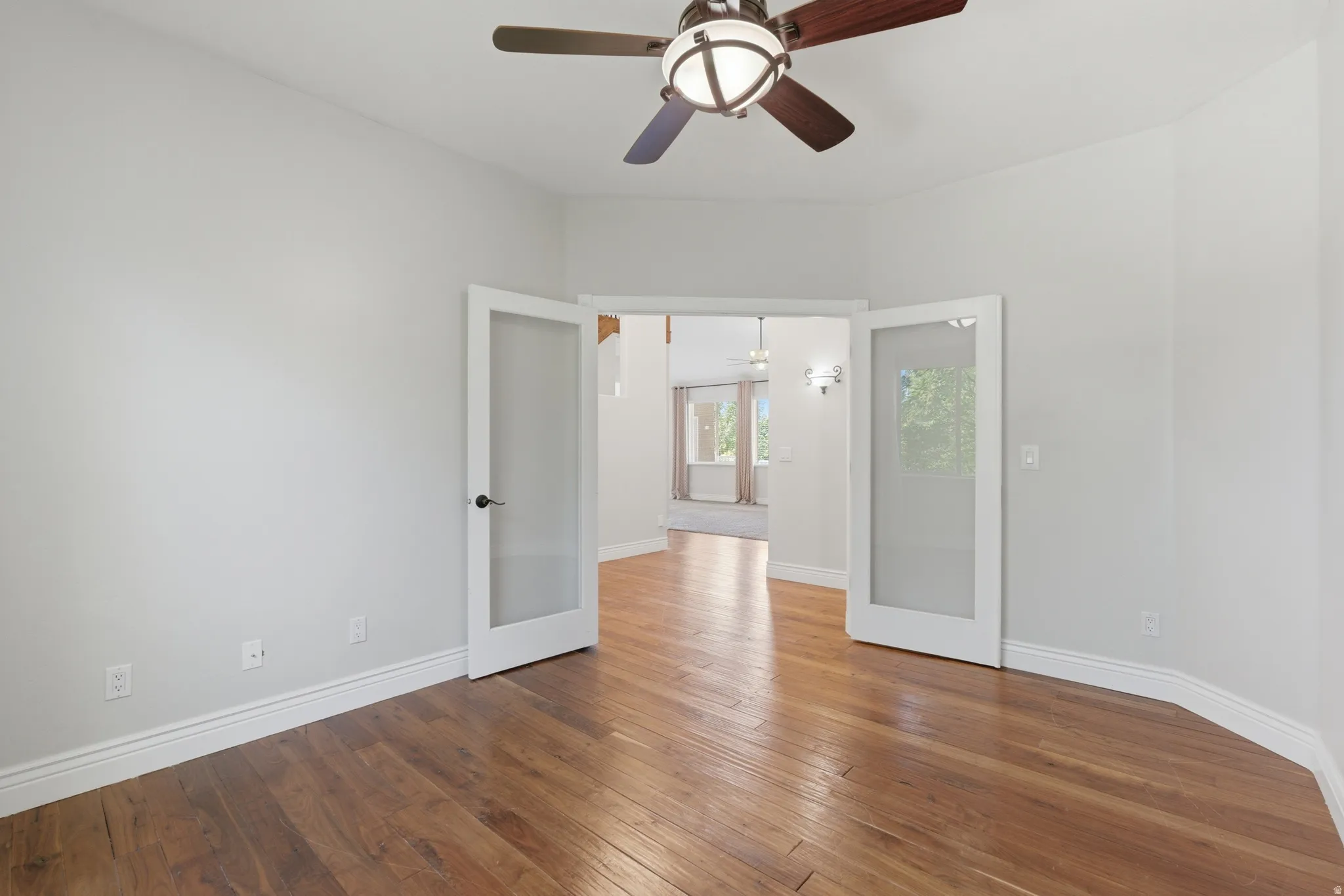 Wood-finish flooring with white baseboards, a ceiling fan with integrated lighting, and double glass-paneled doors