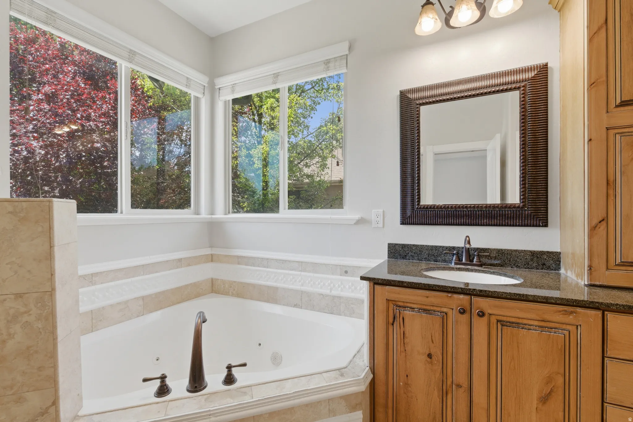 Bathroom featuring a corner soaking tub with tile surround, multi-pane windows, a vanity with wood cabinetry, and a dark stone countertop