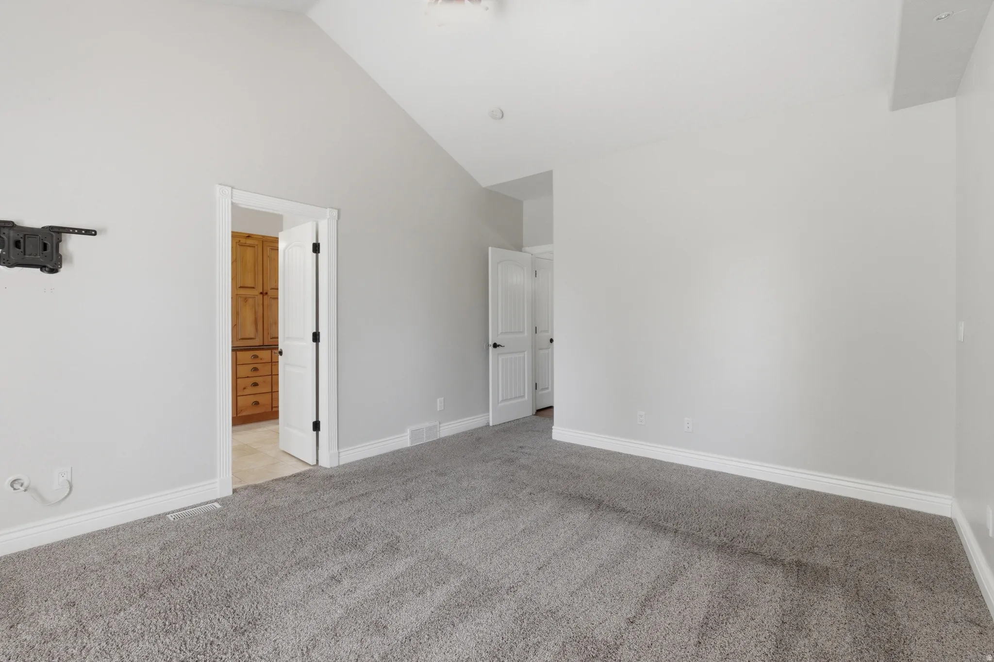 Spacious room featuring vaulted ceilings, light gray wall paint, and gray carpeting