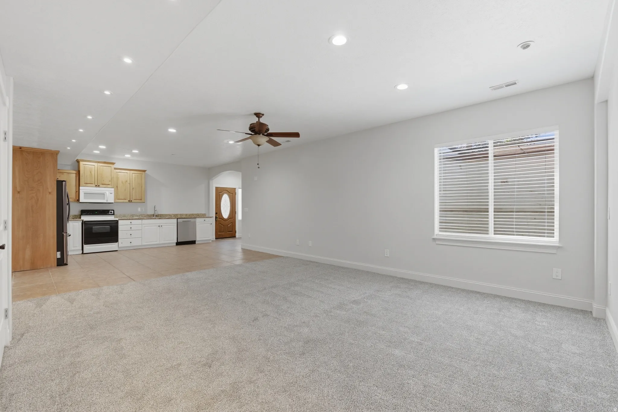 Open concept living area featuring light-toned carpeting and a kitchen with wood-finish cabinetry
