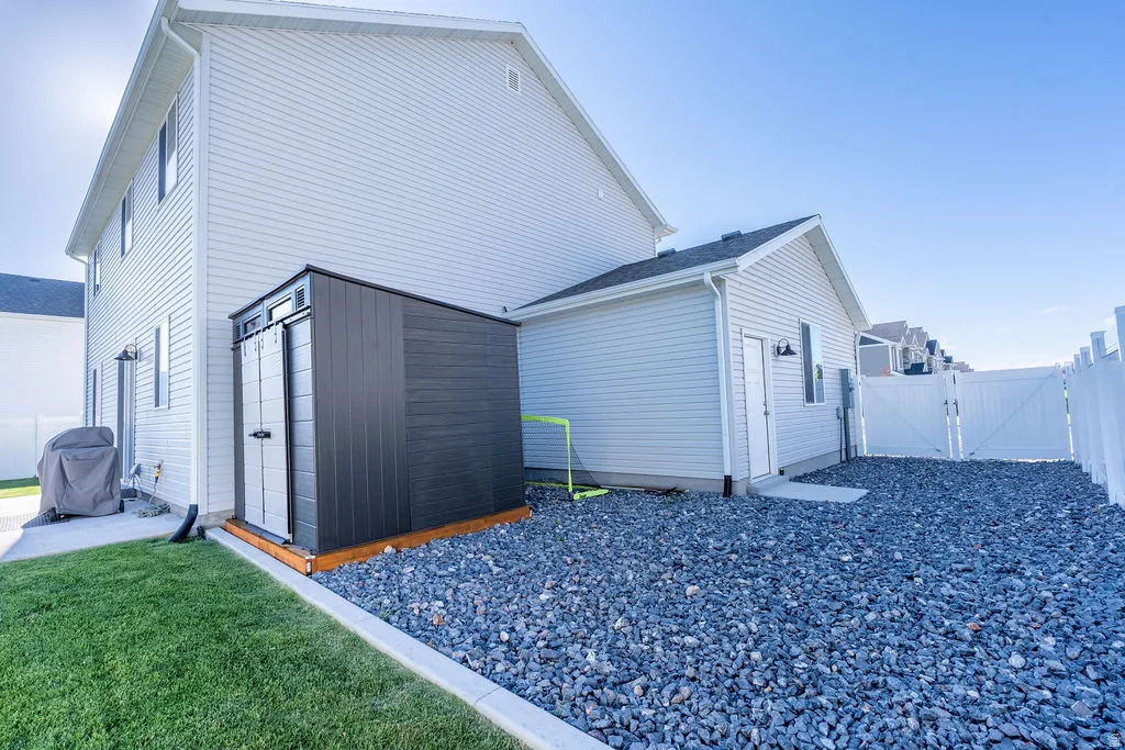 Exterior featuring light-colored siding, a dark storage shed on a wood base, and a gravel-covered area