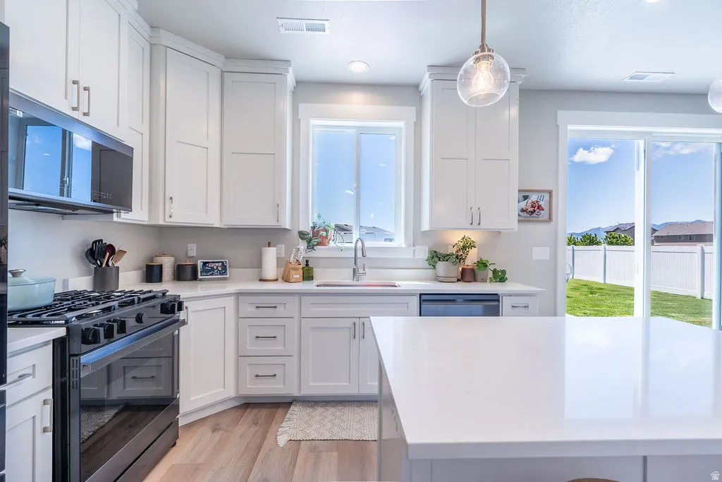 Modern kitchen featuring white shaker cabinetry, light countertops, wood-finish flooring, stainless steel appliances, and a glass sliding door