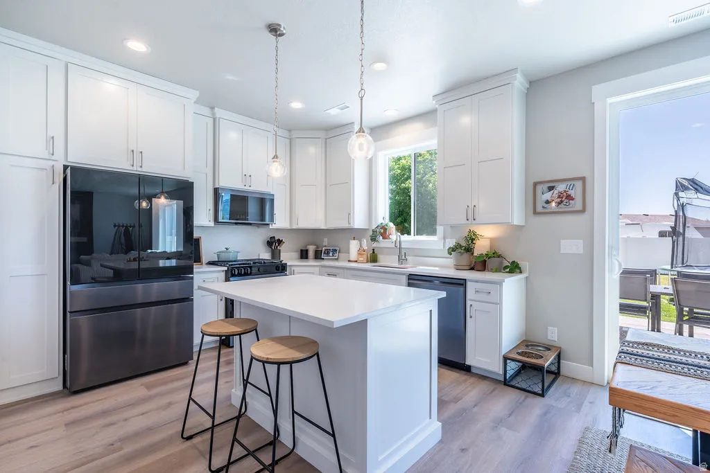 Contemporary kitchen featuring white cabinetry, a central island with countertop seating, stainless steel appliances, wood-finish flooring, and a sliding glass door to an outdoor area