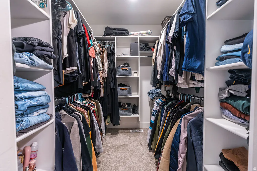 Walk-in closet featuring built-in shelving, multiple hanging rods, and light-toned carpet flooring