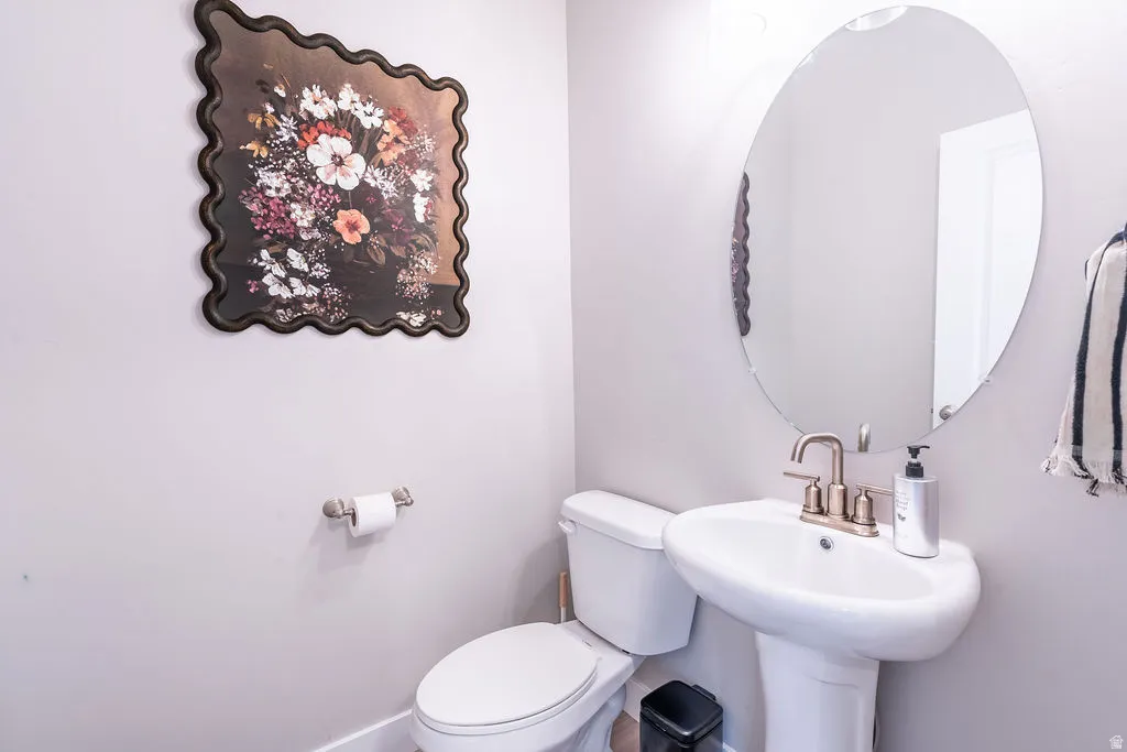 Pedestal sink with a brushed bronze faucet, oval mirror, and white toilet