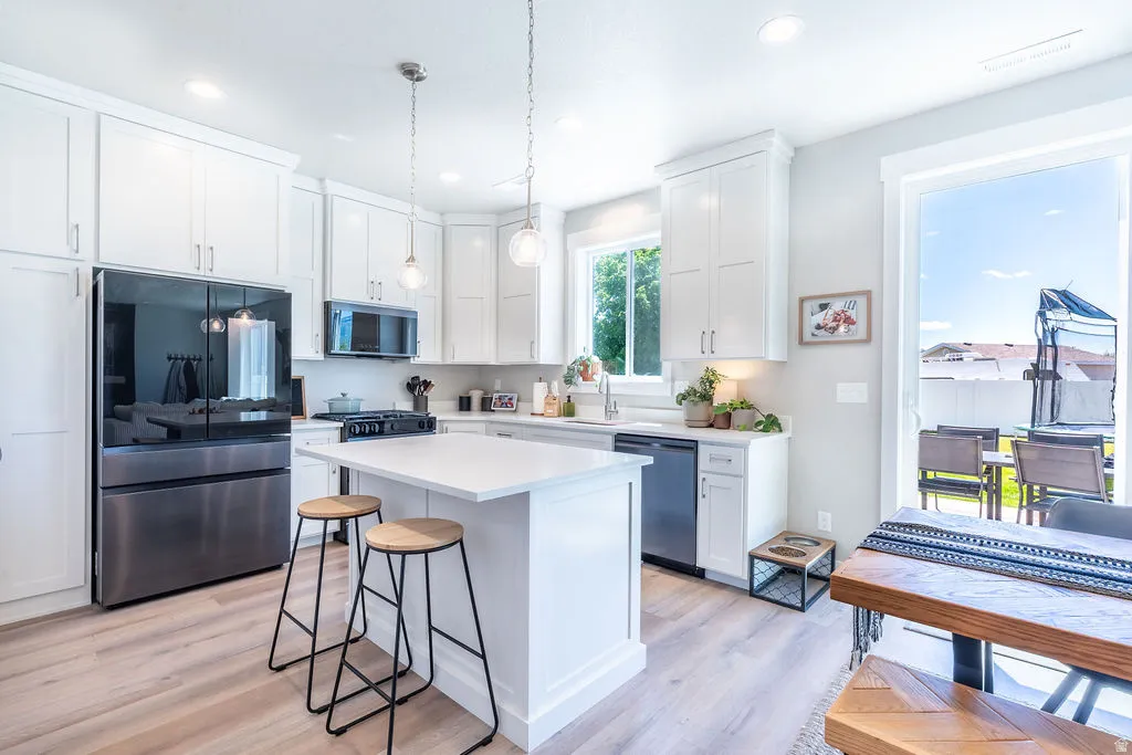 Modern kitchen featuring white cabinetry, a central island with countertop seating, stainless steel appliances, and wood-finish flooring