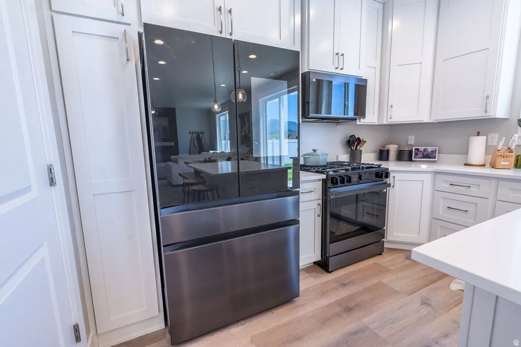 Contemporary kitchen featuring white shaker cabinetry, stainless steel appliances, light wood-finish flooring, and a solid surface countertop