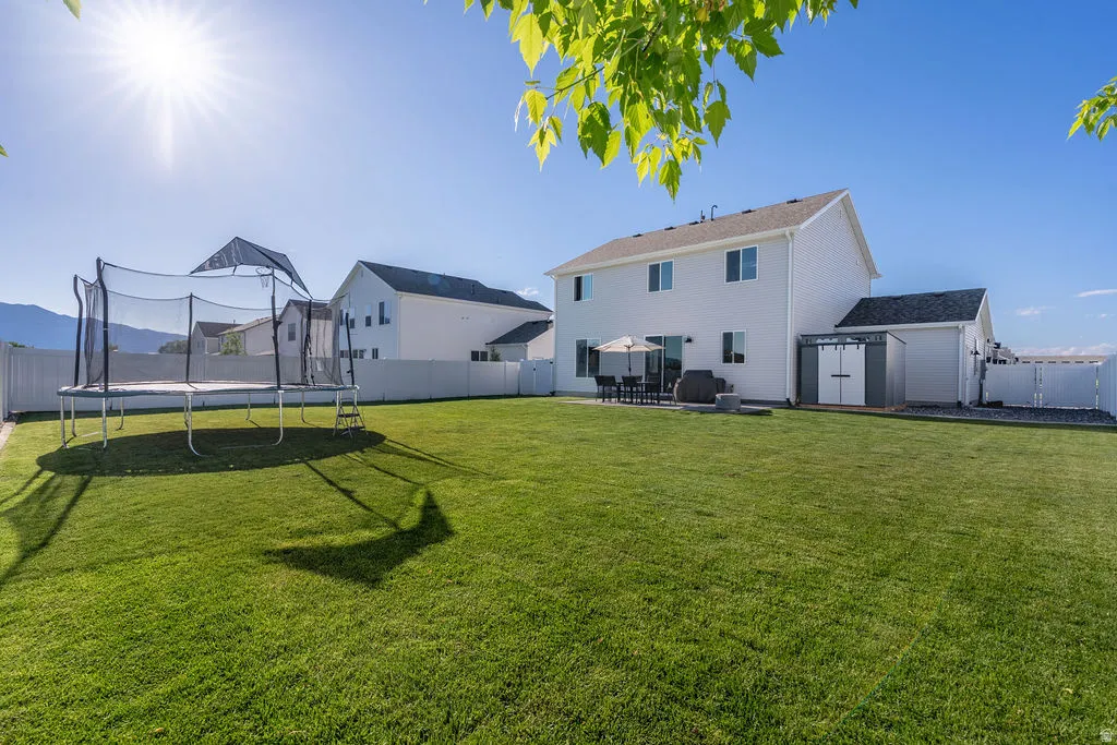 Expansive backyard featuring a large green lawn, full white vinyl fencing, a concrete patio, and a utility shed